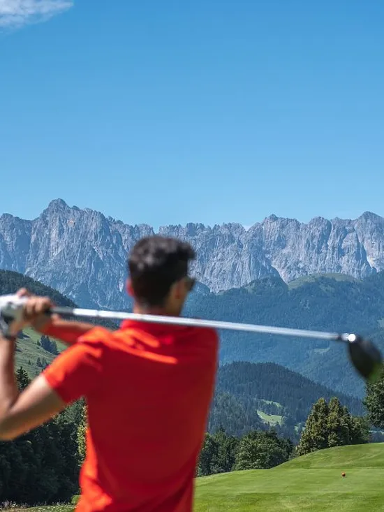 Golfer in red shirt swinging club on mountain golf course in summer